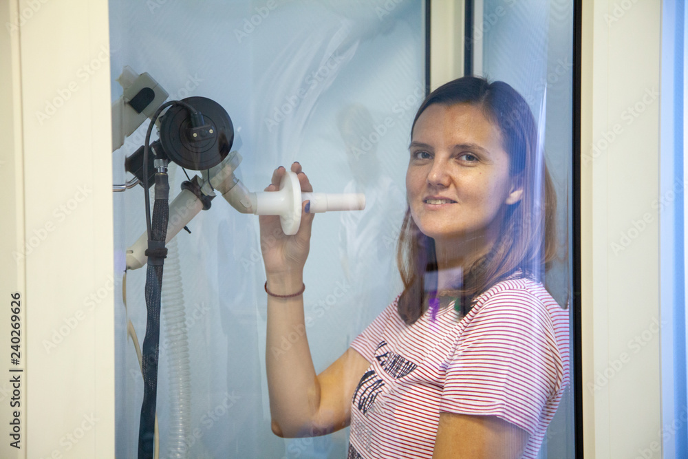 woman sitting in a booth for spirometry with a nose clip on her nose
