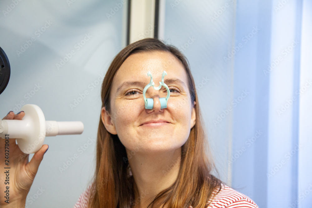 woman sitting in a booth for spirometry with a nose clip on her nose