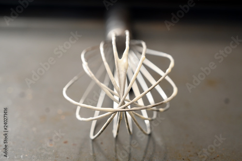 metal wire whisk with dough leftovers on a grey baking tray, close up view with copy space