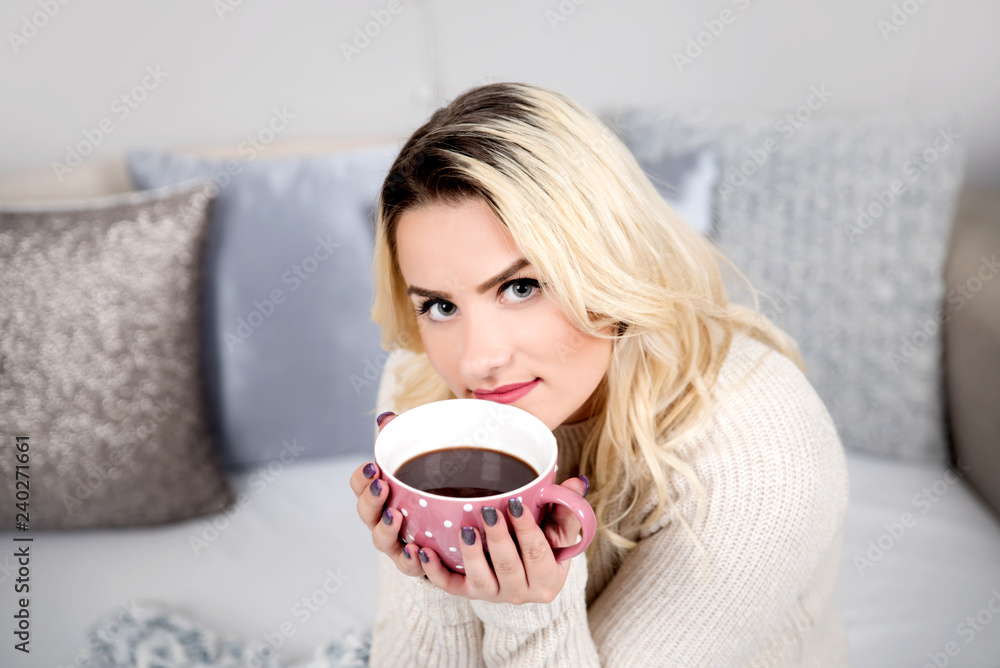 Young woman sitting in bed with cup of coffee