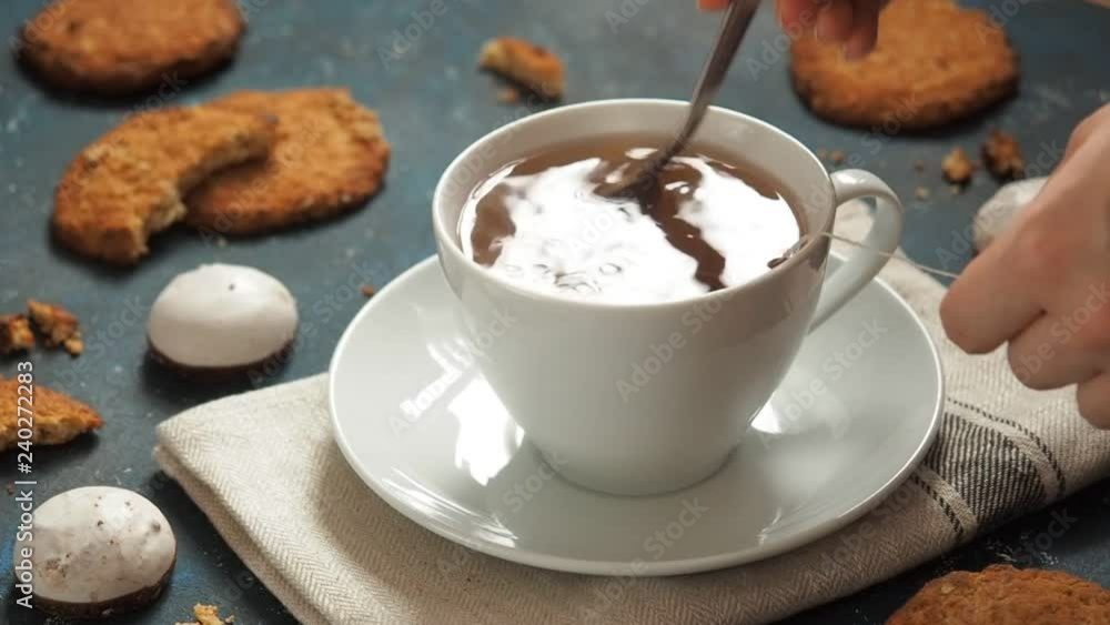 Girl brewing black tea bags in a white cup. Woman stirs water. Still life with cookies on a blue background. Girl brewing black tea bags in a white cup. Woman stirs water. Still life with cookies on a blue background.