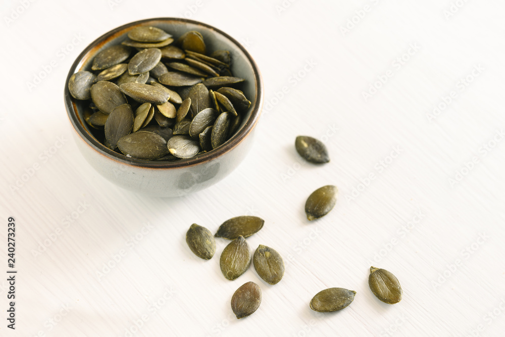 pumpkin seeds in a small bowl on a white table, healthy snack and diet concept, copy space pumpkin seeds in a small bowl on a white table, healthy snack and diet concept, copy space