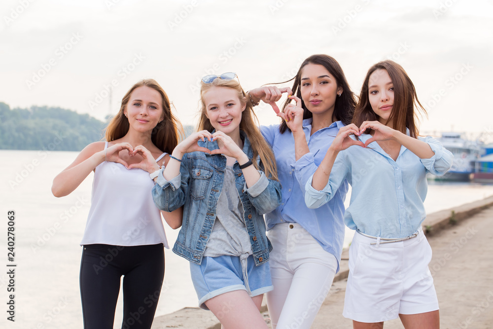Portrait of four young student girls showing finger gesture heart. Beautiful happy young women on the waterfront Portrait of four young student girls showing finger gesture heart. Beautiful happy young women on the waterfront