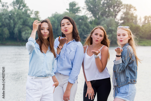 four attractive young women standing and sending kisses at camera outdoor. trees and river at background © liliyabatyrova