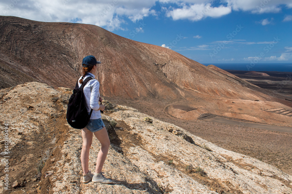 Female tourist with backpack standing on the edge of a volcano enjoying the view on Cladera Blanca, Lanzarote, Spain. 