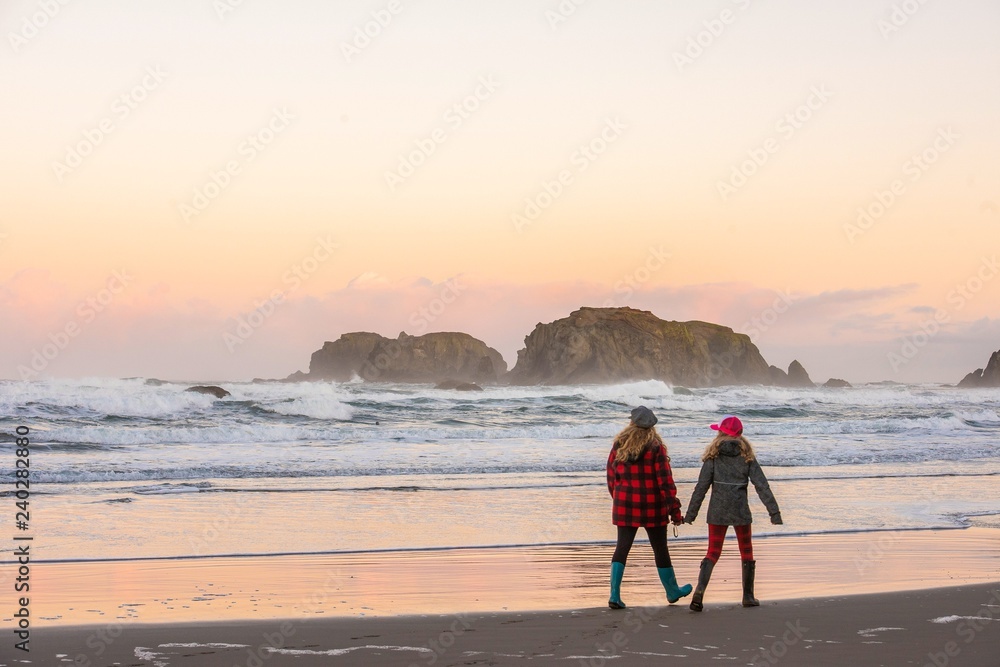 A mother and daughter walking along the beach holding hands at sunrise 
