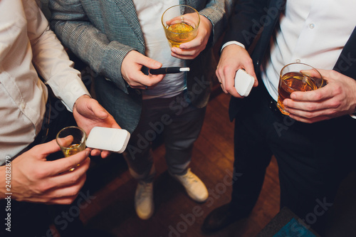 A heat-not-burn tobacco product technology.Man holding in one hand smoking module before smoking. three men are holding alcohol, the concept of smoking electronic cigarettes in the room.