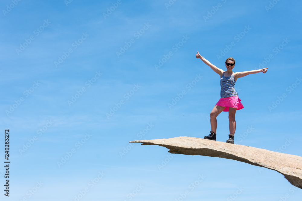 Brave young adult woman hiker stands on top of Potato Chip Rock in San Diego California