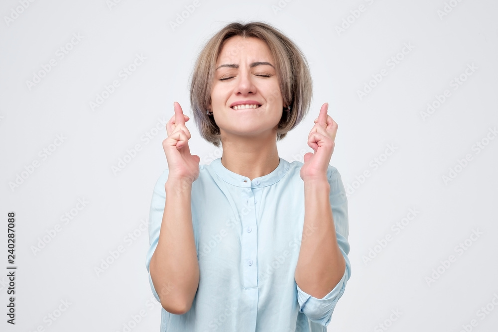 Happy pretty woman eager to win competition, keeps fingers crossed as waits for results, poses in studio. People and wish, desire concept Happy pretty woman eager to win competition, keeps fingers crossed as waits for results, poses in studio. People and wish, desire concept