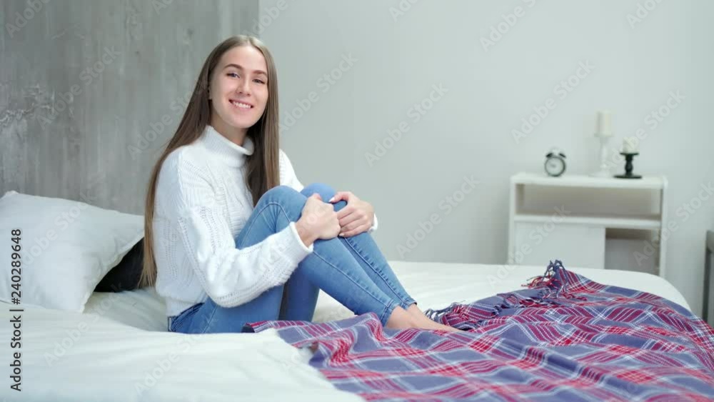 Charming European woman sitting on bed smiling and posing looking at camera Charming European woman sitting on bed smiling and posing looking at camera