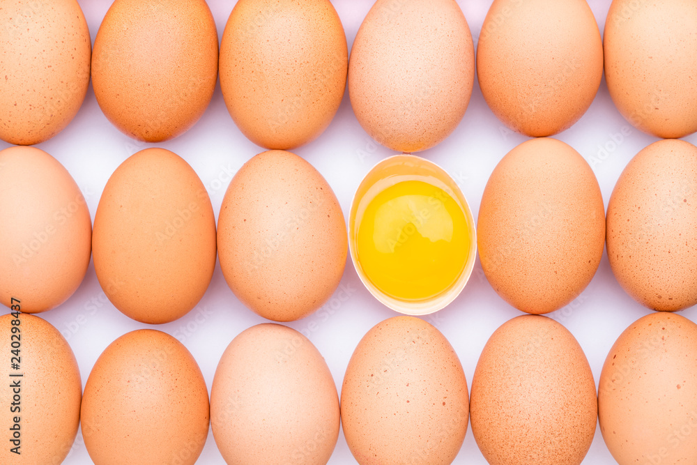 Rows of brown organic eggs and one opened egg with egg yolk on a white background. Rows of brown organic eggs and one opened egg with egg yolk on a white background.