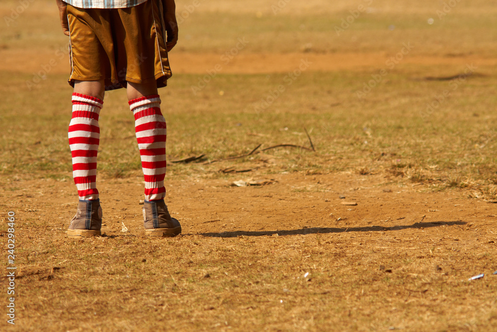 Fototapeta premium Lonely pair of feet of a young football goalie standing on a dusty cricket feet in Mumbai, India