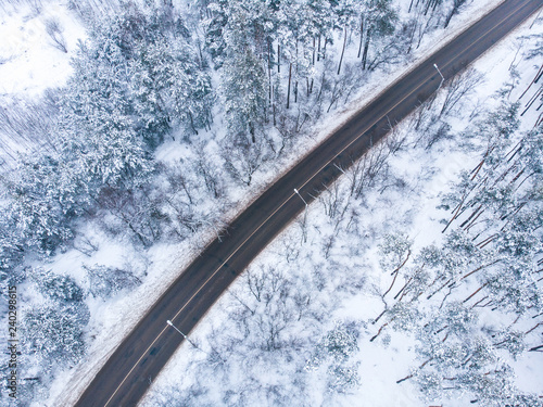 Aerial view of asphalt road among winter landscape in foggy day with frozen forest in snow, drone shot