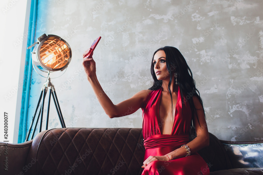 fashion studio photo of gorgeous woman with dark hair and evening makeup,  wears luxurious red dress. neon turquoise lights movie spotlight makes a  selfie Stock-Foto | Adobe Stock