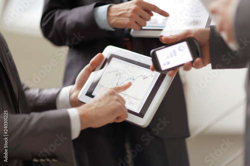 Businessmen at meeting presenting charts on smartphone, tablet