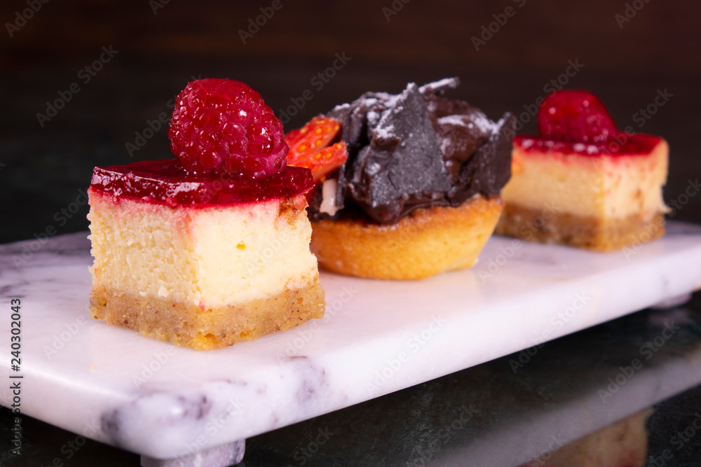 Set of mini cakes in assortment on white plate. Restaurant menu. Blackberry cake with raspberries. Tartlet with fruits. Close up. Set of mini cakes in assortment on white plate. Restaurant menu. Blackberry cake with raspberries. Tartlet with fruits. Close up.