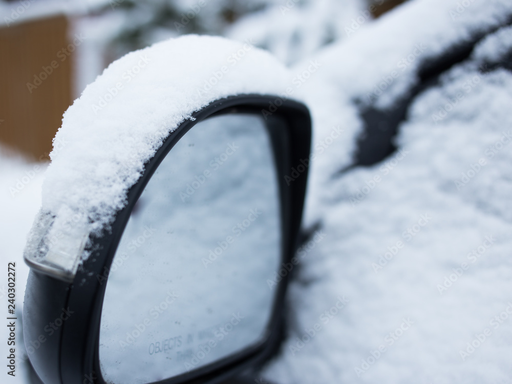 Car's side view mirror of a modern car covered  with snow