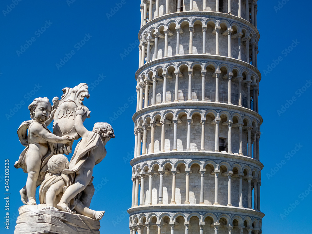 Leaning Tower of Pisa partial view and Putti Fountain sculpture in Piazza dei Miracoli or Square of Miracles in Pisa, Italy against a clear blue summer sky