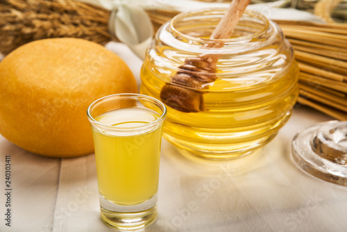Foto Glass of honey liqueur, with cheese and honey jar in background.