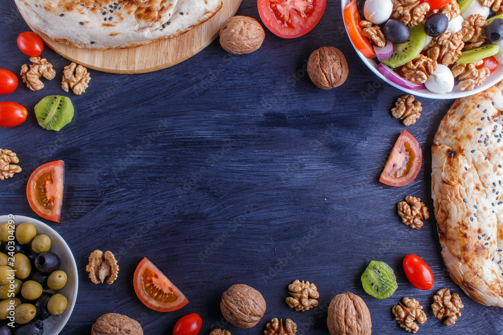 Frame made from tomatoes, mozzarella cheese, olives, kiwi, and walnuts on black wooden background. Frame made from tomatoes, mozzarella cheese, olives, kiwi, and walnuts on black wooden background.
