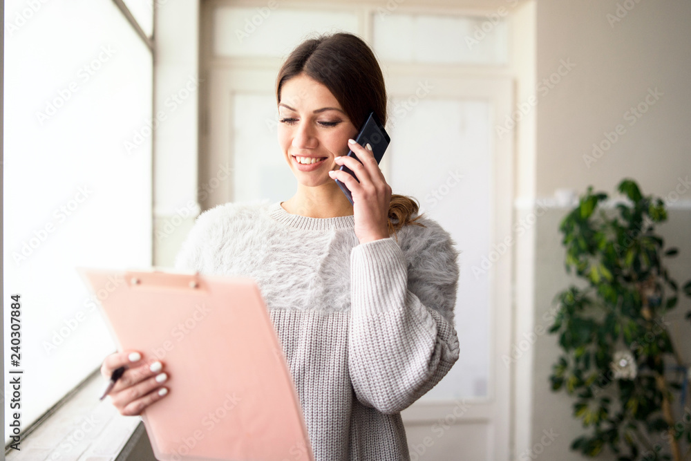 young woman talking on cell phone holding clipboard young woman talking on cell phone holding clipboard