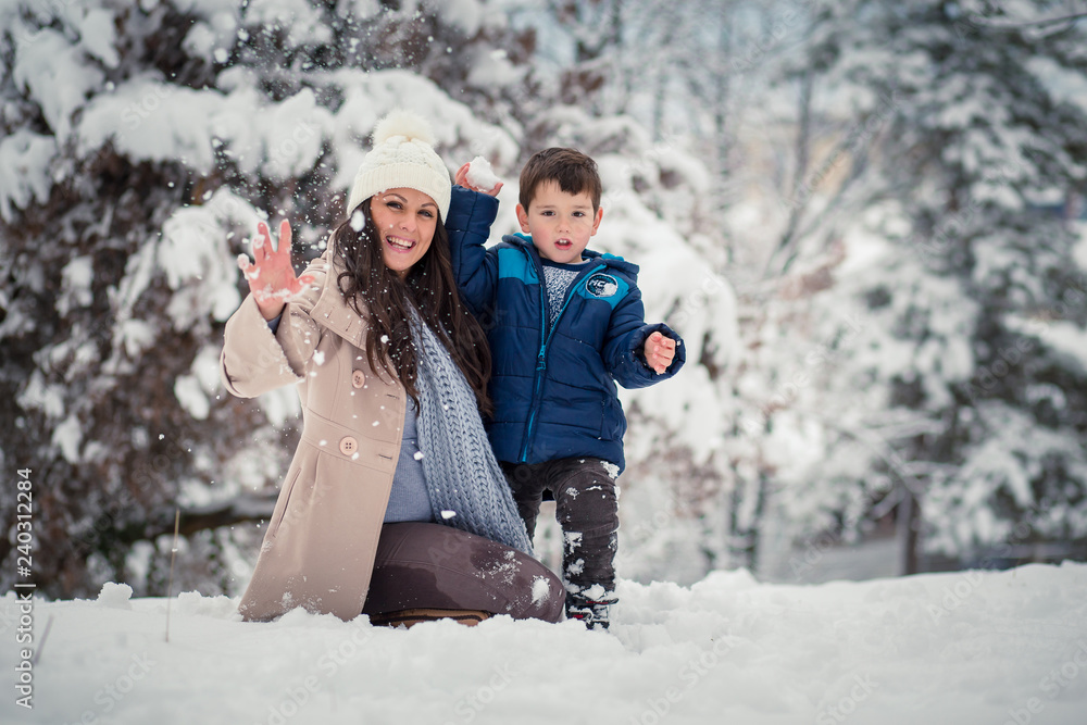 Beatiful mom enjoying winter with her cute, little son, throwing snowballs