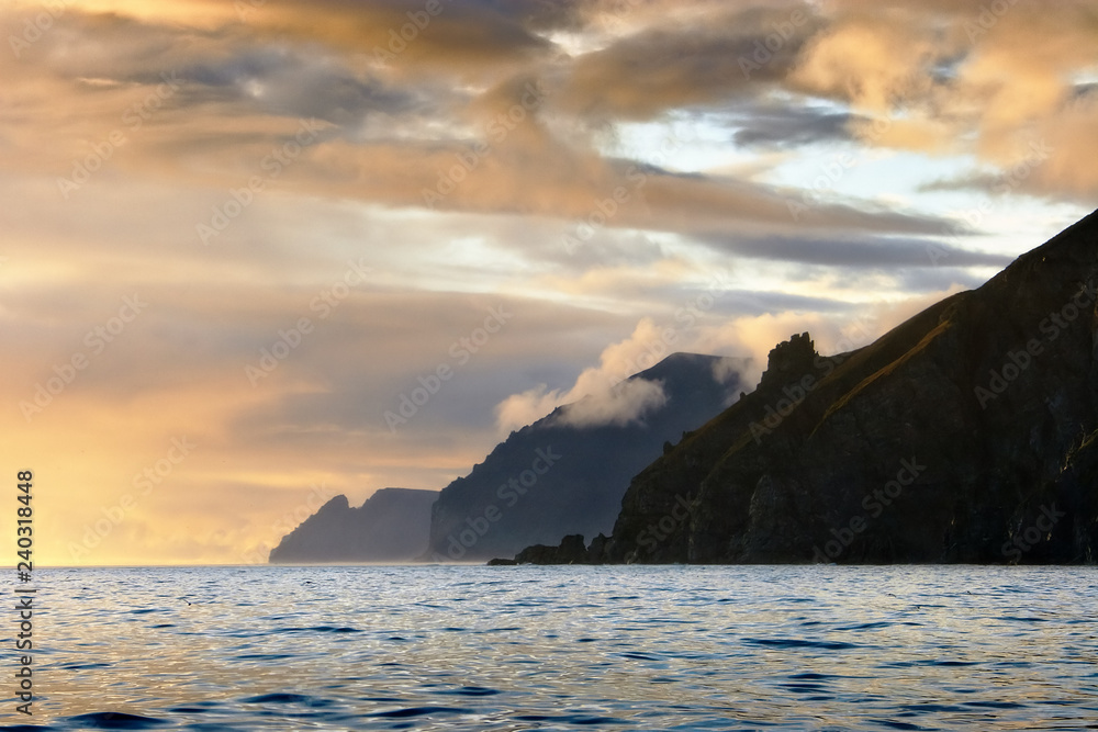 Beautiful sunset on the east coast of Chukotka. Clouds of golden color. Three majestic capes. In the foreground is the Century Cape. Bering Sea, Far East of Russia. Photo can be used for background.