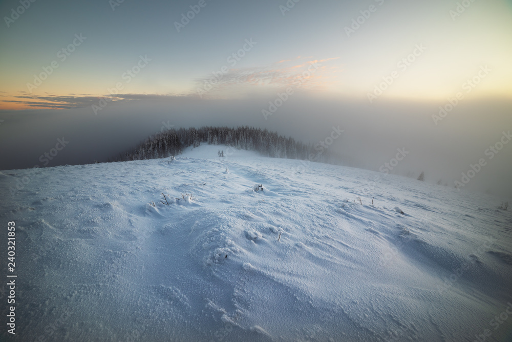 A fabulous winter evening on the Kostrich mountain ridge in the Ukrainian Carpathian Mountains with snow-covered fires, foggy valleys and fantastic skies on the background of a red tent.