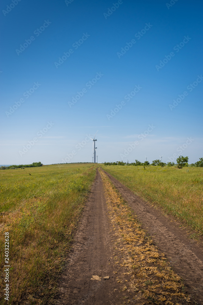 Road between green fields and wind turbines on blue sky background