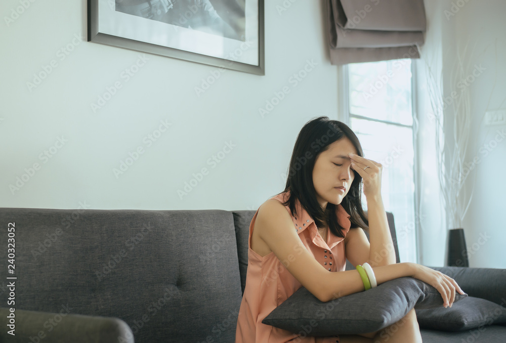 Beautiful young woman sitting on couch at home,Female feeling thoughtful and confused problem,Hold the head with hand,Unexpected pregnancy concept Beautiful young woman sitting on couch at home,Female feeling thoughtful and confused problem,Hold the head with hand,Unexpected pregnancy concept
