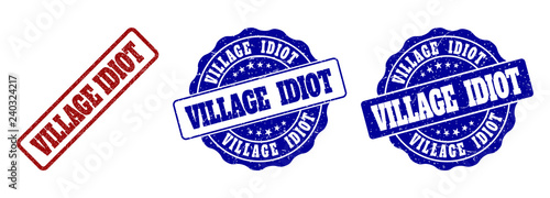 VILLAGE IDIOT scratched stamp seals in red and blue colors. Vector VILLAGE IDIOT labels with dirty style. Graphic elements are rounded rectangles, rosettes, circles and text labels.