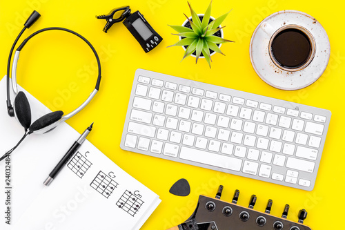 Desk of musician for songwriter work with headphones, keyboard, guitar and notes yellow background top view