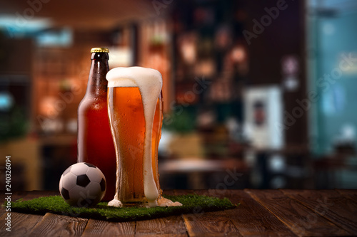Photo of buttle and glass of beer, soccer ball on green grass