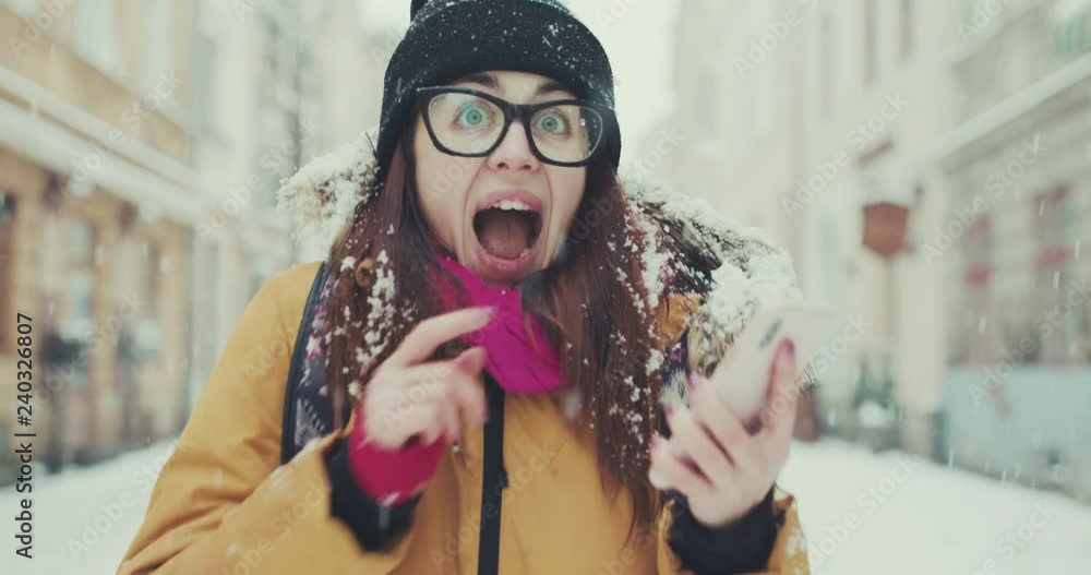 Front view of an excited woman, checking phone and celebrating good news in a winter city street Front view of an excited woman, checking phone and celebrating good news in a winter city street