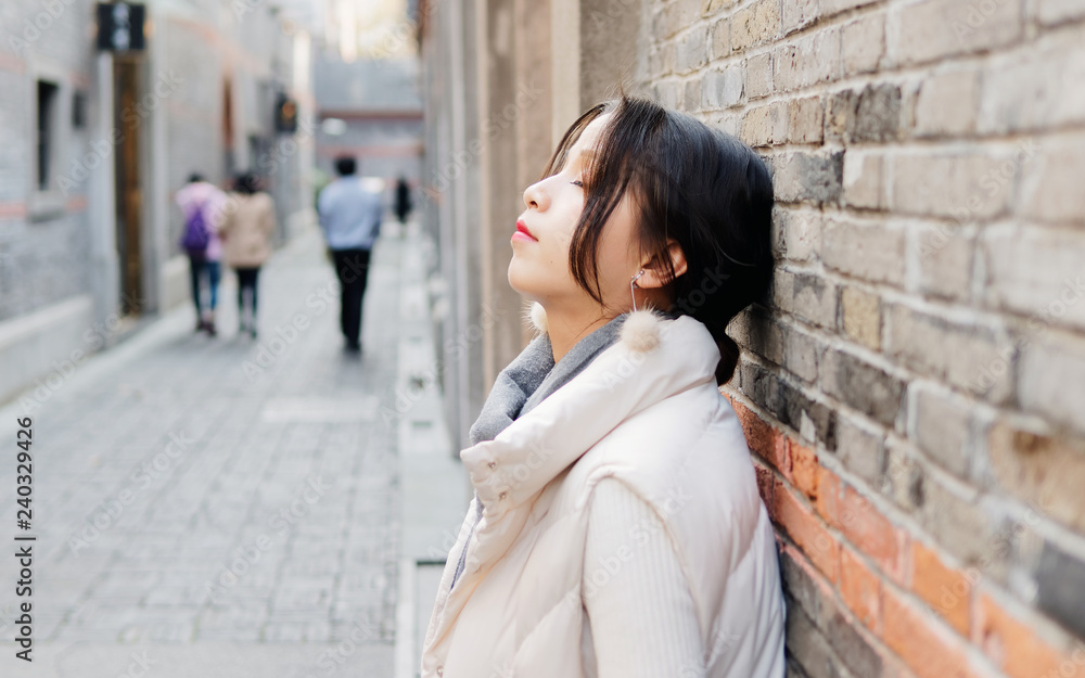 Fototapeta premium Beautiful brunette woman lean against wall with eyes closed in sunny autumn day. Outdoor fashion portrait of glamour young Chinese business stylish lady. Emotions, people, beauty and lifestyle concept
