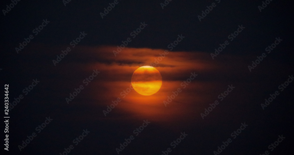 Rising moon through the clouds at dusk