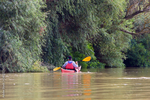 Fototapeta Naklejka Na Ścianę i Meble -  Rear view of teenager paddle red kayak on summer Danube river. Summer kayaking. Concept for adventure, travel, action, lifestyle