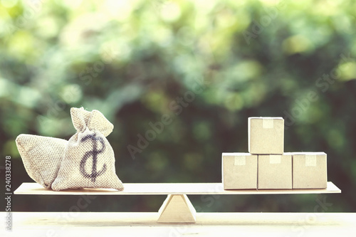 Money dollar bag and supply products on balance scale on wooden table.
