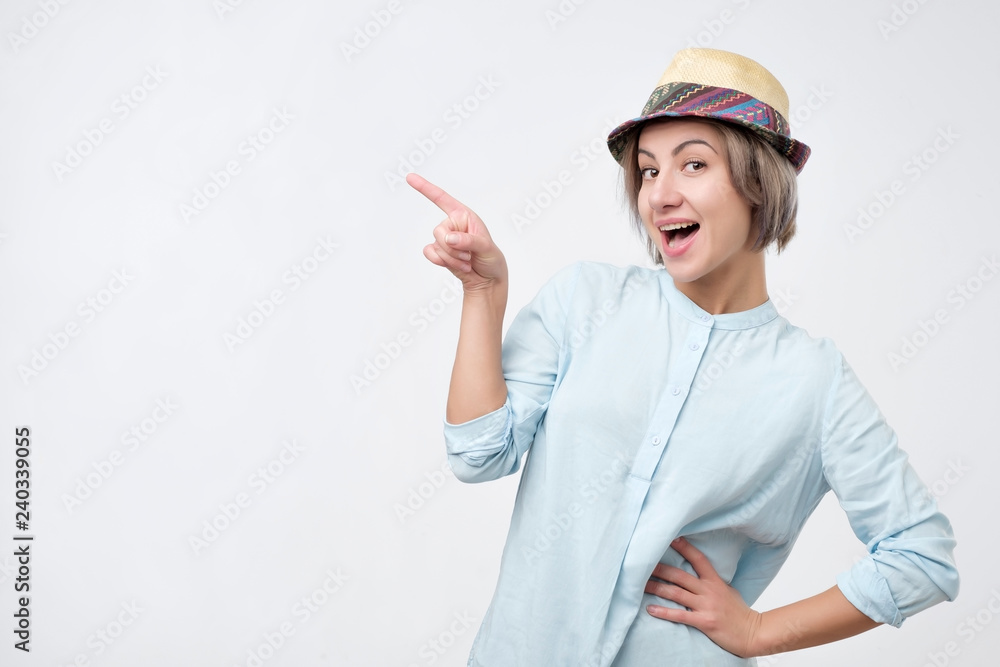 Young attractive woman in summer hat and blue shirt pointing with her finger on copyspace and smiling Young attractive woman in summer hat and blue shirt pointing with her finger on copyspace and smiling