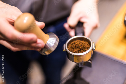 Young Man hands is using a tamper to press freshly ground morning coffee into a coffee tablet