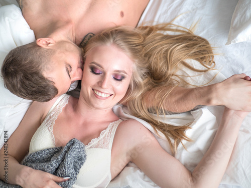 Young couple lying in bed man kissing smiling woman. Love and relationships concept