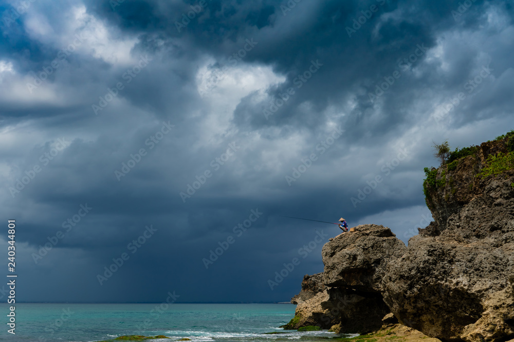 Fisherman catching fish on the rock in the storm 