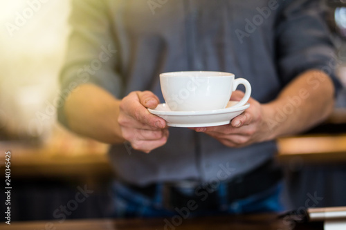 Close up of male barista serving cup of fresh coffee. Cup of coffee in the hands of waiter.