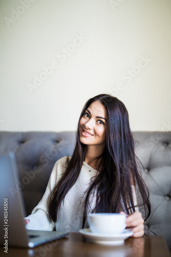 Pretty female student with cute smile keyboarding something on laptop while relaxing after lectures in University. Beautiful happy woman working on laptop computer during coffee break in cafe bar