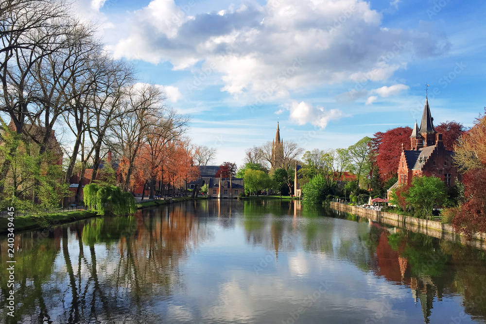 Church on the other side of the lake. Blue sky and blue water on spring day, with reflection in the water. Beautiful colorful landscape of Belgium town Brugge. Outdoors, copy space.