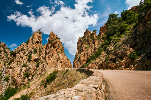 Road through red rock formations of Calanques de Piana in Corsica on sunny summer day