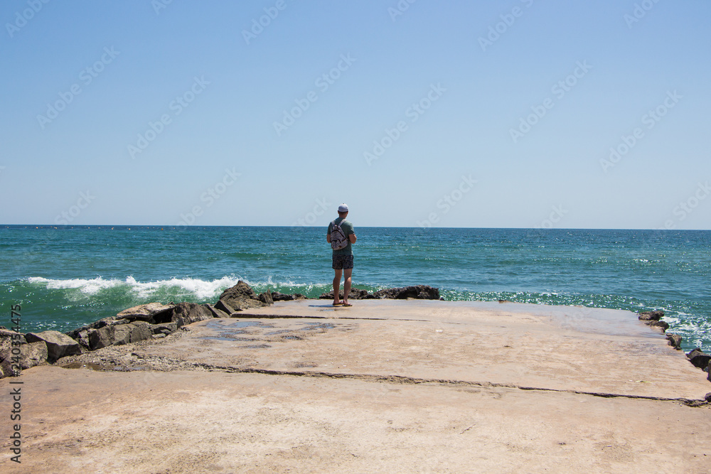 Young boy alone on a pier and waves crash on the rock 