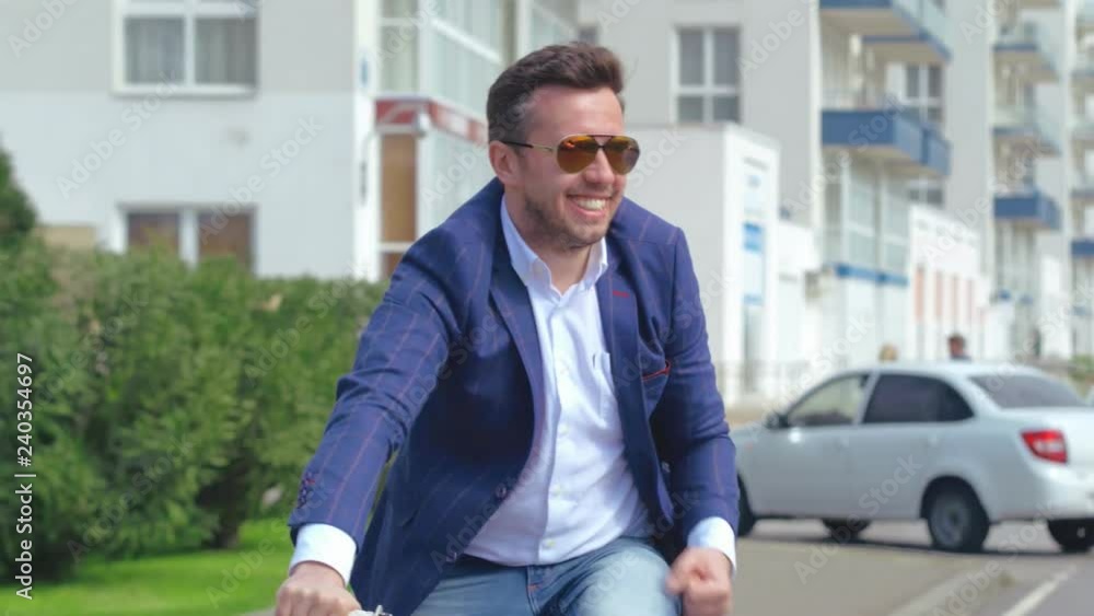 Cheerful businessman riding on bicycle on city street and showing yes gesturing Cheerful businessman riding on bicycle on city street and showing yes gesturing