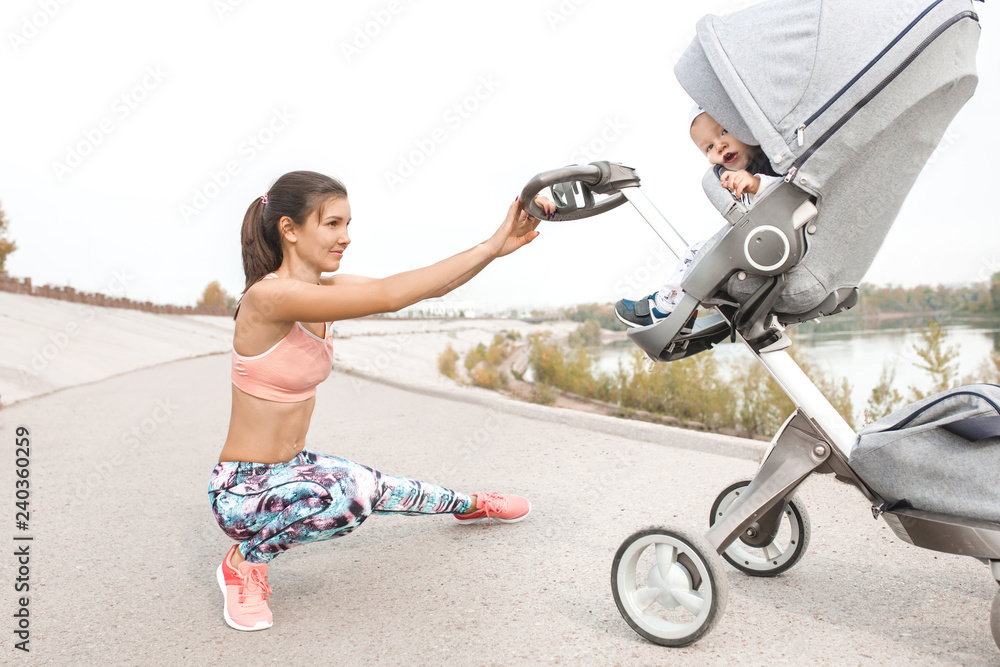 Active mother jogging. Jogging or power walking woman with pram at sunset. mom squats while walking with baby in stroller Active mother jogging. Jogging or power walking woman with pram at sunset. mom squats while walking with baby in stroller