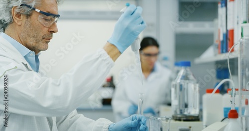 Portrait of male scientist with a pipette analyzes a liquid to extract the DNA and molecules in the test tubes in laboratory. Concept: research,biochemistry, pharmaceutical medicine